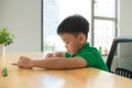 Asia little student boy studying and doing his homework at home, on the table, home education, thinking action Royalty Free Stock Photo