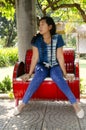 Asia thai woman travel visit and sitting on red metal bench posing for take photo in public garden park Royalty Free Stock Photo