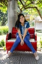 Asia thai woman travel visit and sitting on red metal bench posing for take photo in public garden park Royalty Free Stock Photo