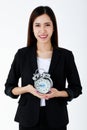 Asian adorable business woman with long hair wearing formal black suit, smiling, looking and holding alarm clock with isolated Royalty Free Stock Photo