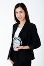 Asian adorable business woman with long hair wearing formal black suit, smiling, looking and holding alarm clock with isolated Royalty Free Stock Photo