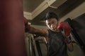 Young handsome and fierce teenager boy doing fight workout punching heavy bag looking cool and badass at fitness club training