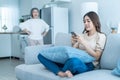 Asian angry senior mature woman shouting at stubborn fussy daughter. Young female sit on sofa use mobile phone chat, disobedient Royalty Free Stock Photo