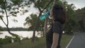 Asian athlete woman in green nature tree park and lake in evening sunset feeling thirsty drink water from bottle. energy drinks