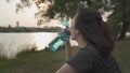 Asian athlete woman in green nature tree park and lake in evening sunset feeling thirsty drink water from bottle. energy drinks