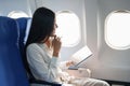 Asian attractive business woman passenger sitting on business class luxury plane while tablet computer while travel