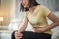 Asian attractive girl with painful face, clasping belly feel suffer from severe abdominal pain. Stressed young woman sit on sofa a