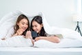 Asian attractive lesbian couple use mobile phone watch movie on bed. Beautiful sibling in pajamas lying down with blanket in Royalty Free Stock Photo