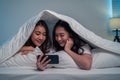 Asian attractive lesbian couple use mobile phone watch movie on bed. Beautiful sibling in pajamas lying down with blanket in Royalty Free Stock Photo