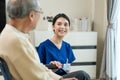 Asian attractive nurse taking care of mature senior elderly male patient sitting on wheelchair at home nursing care. Happy
