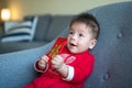Baby boy holding a red pocket envelope for Lunar New Year sitting on a sofa at home Royalty Free Stock Photo