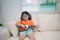 Asian baby girl child wearing glasses and headphone learning small guitar online study online on sofa in living room at home. Royalty Free Stock Photo