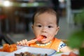 Asian baby girl in restaurant with a spoon eats food Royalty Free Stock Photo