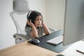 Asian baby girl wearing headphone to listen music or using white keyboard laptop and study online on wood table desk in living Royalty Free Stock Photo