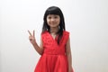 Asian baby girl wearing red dress showing victory hand sign or number two with her fingers, looking at camera and smiling happy Royalty Free Stock Photo