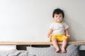Asian baby with pacifier in her mouth is sitting on the bed in bedroom Royalty Free Stock Photo