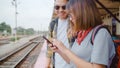 Asian backpack couple at train station, Young sweet couple tourist backpacker using mobile phone looking and direction maps on