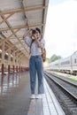 Asian backpack traveler woman with camera standing at train station platform and waiting train arrivel, summer holiday Royalty Free Stock Photo