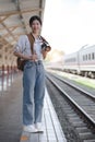 Asian backpack traveler woman with camera standing at train station platform and waiting train arrivel, summer holiday Royalty Free Stock Photo