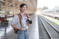 Asian backpack traveler woman with camera standing at train station platform and waiting train arrivel, summer holiday Royalty Free Stock Photo