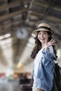 Asian backpack traveler woman smiling and waving hand at train station platform