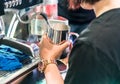 Asian barista steaming fresh milk in stainless pitcher with vent