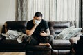 Asian bearded man sit on couch in living room at home. Looking at cell phone