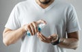 Asian bearded man in white shirt standing over grey background using rubbing alcohol portable spraying on his palms and hands Royalty Free Stock Photo