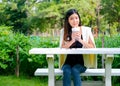 Asian beautiful business girl drink some water from a cup and sit in the green garden with concept of work with green environment Royalty Free Stock Photo