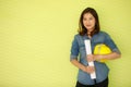 Asian beautiful female engineer carrying white paper roll and holding yellow safty helmet