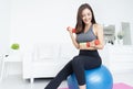 Asian beautiful girl working out with dumbbells sitting on gymnastic blue fit ball in living room at her home. Sport, fitness, Royalty Free Stock Photo