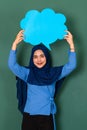 Asian beautiful happy smiley Muslim woman wearing blue hijab standing confidently and holding blue copy space speech bubble over Royalty Free Stock Photo