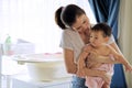 Asian beautiful mother holding little cute baby after taking a bath and looking and her child standing in the room. Bathtub and Royalty Free Stock Photo