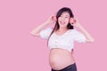 Asian beautiful pregnant woman stands relaxed and enjoys listening to music on headphones connected to the internet