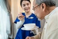 Asian beautiful therapist doctor serve food to older patient in house. Young woman nurse at nursing home taking care of disabled Royalty Free Stock Photo