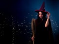 Asian beautiful woman wear witch costume include red magic hat and cloak while holding natural broom in the dark blue background