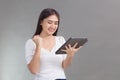 Asian beautiful woman in white shirt is show victory smiling happily and satisfy while look at on tablet in her hand on grey