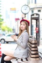 Asian beautiful woman who wears suit and red cap with bronze hair sits on chair in the city outdoors while holds coffee cup in her Royalty Free Stock Photo