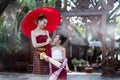 Asian beautiful woman wear a luxury national costume and holding a red umbrella and a little girl standing in classic thai house Royalty Free Stock Photo