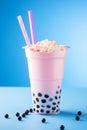 Asian boba tapioca pink bubble tea with cream topping on blue background, vertical photo.