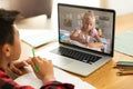 Asian boy with book and pencil looking at caucasian girl over laptop screen during online class Royalty Free Stock Photo