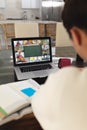 Asian boy with books on table attending online lecture over video call on laptop at home Royalty Free Stock Photo