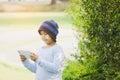 Asian boy with cute, wearing a hat, with looking tablet in hand, standing in garden with lush greenery, online learning concepts