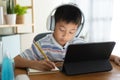 Asian boy learning online via internet with a tutor on a tablet digital with headphone, Asia child is studying while sitting in Royalty Free Stock Photo