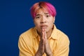 Asian boy with pink hair frowning while payer gesture