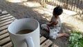 Asian boy playing alone digging sand with bare hands on the sandy shore. A coffee mug on a bamboo table obscures the view.