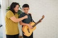 Asian boy playing guitar and mother sing a song and embrace, feel appreciated and encouraged. Concept of a happy family, learning