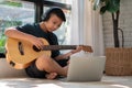 Asian boy playing guitar and watching online course on laptop while practicing for learning music or musical instrument online at Royalty Free Stock Photo