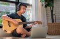 Asian boy playing guitar and watching online course on laptop while practicing for learning music or musical instrument online at Royalty Free Stock Photo