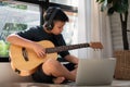 Asian boy playing guitar and watching online course on laptop while practicing for learning music or musical instrument online at Royalty Free Stock Photo